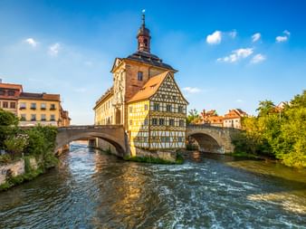 Bambergs historisches Altes Rathaus, ein Fachwerkgebäude auf einer Brücke über die Regnitz, mit bunten Fassaden und Turm unter blauem Himmel.
