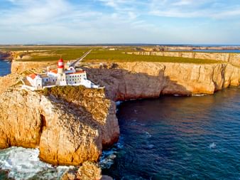 Luftaufnahme des Leuchtturms Cabo de São Vicente mit rot-weißem Turm auf dramatischen goldenen Klippen im Atlantik.