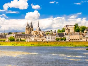 Blick auf Blois über die Loire mit historischen Gebäuden und Kirchtürmen unter blauem Himmel mit weißen Wolken.