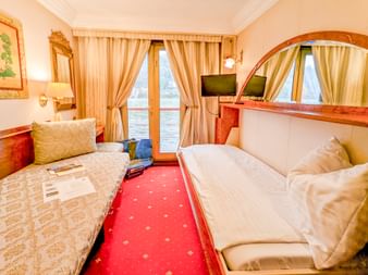 Oberdeck-Kabine auf der MS Prinzessin Katharina mit ausgeklapptem Bett, Schlafsofa, rotem Teppich, Holzmöbeln, Spiegel, TV und Fenster mit Wasserblick.