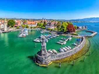 Luftaufnahme des Lindauer Hafens am Bodensee mit Löwenstatue auf Steinmole, Booten im Hafen, historischer Altstadt mit bunten Gebäuden und Kirchturm.