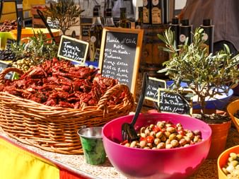 Bunter provenzalischer Marktstand mit Weidenkorb voller getrockneter Tomaten, Schalen mit marinierten Oliven, Olivenzweigen und Olivenöl.