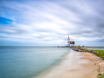 Langzeitbelichtung eines Leuchtturms auf einem Steinkai in Marken, Niederlande, mit Sandstrand und bewölktem Himmel.