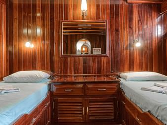 Zweibettkabine auf der MS Thalassa mit zwei Einzelbetten, Holzverkleidung, Nachttisch mit Spiegel und Wandlampen. Blaue Bettwäsche.