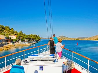 Blick vom Sonnendeck der MS Sveti Vid mit Passagieren, die die kroatische Küste mit blauem Wasser, Küstendorf und Hügeln genießen.
