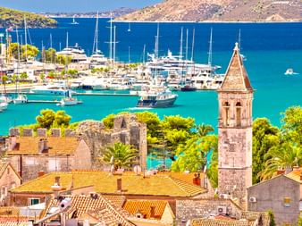 Luftaufnahme der Altstadt von Trogir mit Steinturm, Terrakottadächern und türkisfarbener Marina voller Yachten vor Küstenhügeln.