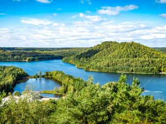 Luftaufnahme von blauen Seen umgeben von dichten grünen Wäldern im Nationalpark Hoge Kempen unter teilweise bewölktem Himmel.