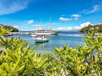 Malerische Bucht in Korcula mit türkisfarbenem Wasser, kleinen Booten und einer weißen Yacht. Grüne Vegetation rahmt die Aussicht ein.
