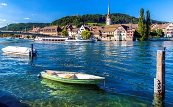 Historische Stadt Stein am Rhein mit bunten Gebäuden, Kirchturm und Booten auf dem Rhein unter blauem Himmel.