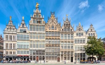 Reihe prächtiger Gildehäuser mit Treppengiebeln und goldenen Statuen in Antwerpen. Menschen entspannen auf dem Kopfsteinpflasterplatz.
