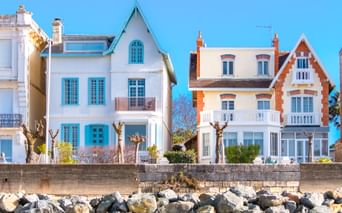 Reihe bunter Strandhäuser in Royan mit weißen und türkisfarbenen Fassaden und markanter Architektur. Felsiger Strand im Vordergrund.