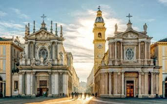 Piazza San Carlo in Turin mit barocken Zwillingskirchen an einer zentralen Straße. Ein goldener Glockenturm erhebt sich zwischen ihnen.
