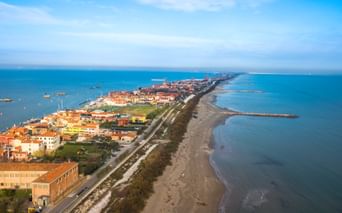 Luftaufnahme von Pellestrina, einer schmalen Insel mit bunten Gebäuden entlang einer Küstenstraße zwischen der Adria und der Lagune von Venedig.