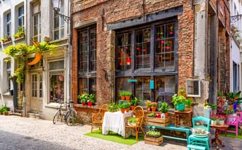 Charmanter Blumenladen mit Backsteinfassade in Antwerpen. Bunte Pflanzen und Möbel auf Kopfsteinpflaster mit Fahrrad in der Nähe.