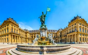 Panoramablick auf die Würzburger Residenz, ein prächtiger Barockpalast mit gelber Fassade und prunkvollem Brunnen im Innenhof.