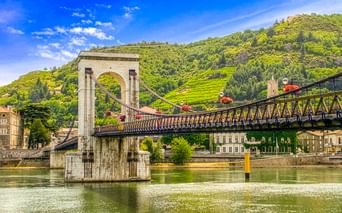 Passerelle Marc Seguin Hängebrücke über die Rhône in Tournon, mit grünen Weinbergen am Hang und historischen Gebäuden im Hintergrund.