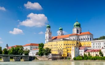 Passau old town with St. Stephen's Cathedral featuring green onion domes along the Inn river. Colorful historic buildings line the waterfront.