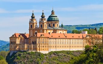 Stift Melk, ein gelbes Barockkloster mit Zwillingstürmen und grüner Kuppel, thront auf einem Felsen über dem Donautal in Österreich.