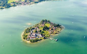 Luftaufnahme der Fraueninsel, einer kleinen Insel im bayerischen Chiemsee mit historischen Gebäuden, grünen Wiesen und Bäumen, umgeben von türkisfarbenem Wasser.