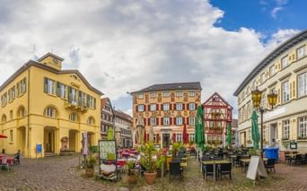 Kopfsteinpflaster-Marktplatz in Eberbach mit bunten Fachwerkhäusern, Außengastronomie und gelbem Rathaus unter bewölktem Himmel.