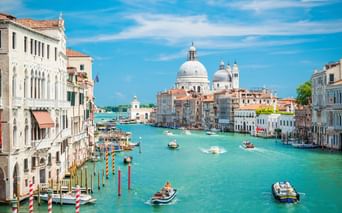 Venedigs Canal Grande mit türkisfarbenem Wasser, Booten und bunten Gebäuden. Die weiße Kuppelbasilika Santa Maria della Salute dominiert den Hintergrund.