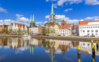 Historische Lübecker Altstadt am Wasser mit bunten Gebäuden und Kirchtürmen, die sich im ruhigen Wasser unter blauem Himmel spiegeln.