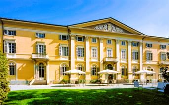 Gelbe neoklassizistische Villa Matilde mit weißen Säulen und dekorativem Giebel in Romano Canavese. Terrasse mit weißen Sonnenschirmen.