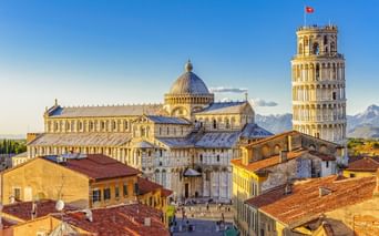 Luftaufnahme des Domplatzes von Pisa mit dem Schiefen Turm, dem Dom mit Kuppel und umliegenden historischen Gebäuden mit Terrakottadächern.
