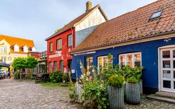 Kopfsteinpflasterstraße in Steges Altstadt mit bunten historischen Häusern: blaue, rote und gelbe Gebäude mit Ziegeldächern und Blumenkübeln.