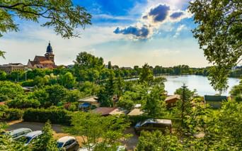 Blick auf Waren mit St. Marien Kirchturm und Tiefwarensee, eingerahmt von grünen Bäumen. Boote und Gebäude am Ufer sichtbar.