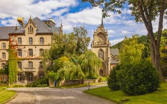 Historisches Zisterzienserkloster Schulpforte mit Kirchturm und Wohngebäuden, umgeben von grünen Rasenflächen und Bäumen unter blauem Himmel.
