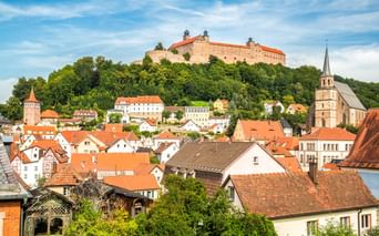 Plassenburg auf einem Hügel über der Stadt Kulmbach mit rotgedeckten Häusern, Kirchturm und grünen Bäumen unter blauem Himmel in Franken.