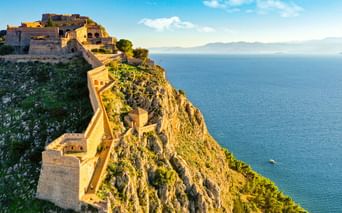 Festung Palamidi in Nafplio auf einer steilen Klippe mit Blick auf das blaue Meer. Steinbefestigungen schlängeln sich den felsigen Hang hinunter.