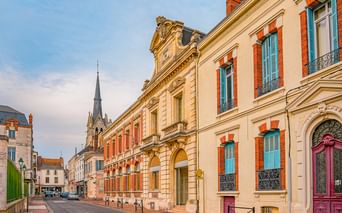 Straßenansicht der Altstadt von Montargis mit farbenfrohen historischen Gebäuden mit türkisfarbenen Fensterläden, verzierten Fassaden und Kirchturm.