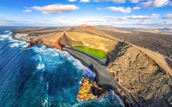 Aerial view of El Golfo's bright green lagoon surrounded by volcanic crater, black sand beach, and turquoise ocean on Lanzarote, Spain.