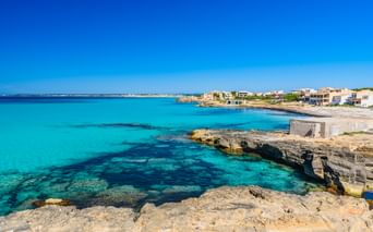 Türkisfarbene Mittelmeerbucht mit felsiger Kalksteinküste und weißen Gebäuden im Hintergrund unter klarem blauen Himmel in Spanien.