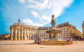 Place de la Bourse in Bordeaux mit prächtigem Brunnen in der Mitte des Kopfsteinpflasterplatzes, umgeben von klassischen Gebäuden aus dem 18. Jahrhundert.