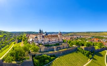 Luftaufnahme der Festung Marienberg in Würzburg, umgeben von Weinbergen und Festungsmauern, mit Blick auf die Stadt und das Flusstal.