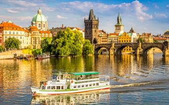 Touristenboot auf der Moldau mit Karlsbrücke und Prager Altstadt mit bunten Gebäuden, Kirchenkuppeln und Türmen.