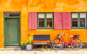 Rotes Fahrrad mit Korb vor gelbem Haus mit grüner Tür und rosa Fensterläden im Kopenhagener Stadtteil Nyboder.