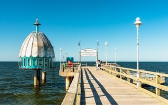 Hölzerne Seebrücke in Zinnowitz, die in die Ostsee führt, mit einer markanten türkis-weißen Tauchgondel auf der linken Seite.