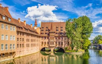 Historisches Heilig-Geist-Spital mit Bogenbrücke über die Pegnitz in Nürnberg, umgeben von traditionellen Gebäuden und Bäumen.