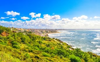 Panoramablick auf die Küste von Figueira da Foz mit grünem Hang, Sandstrand und Atlantik unter blauem Himmel mit weißen Wolken.