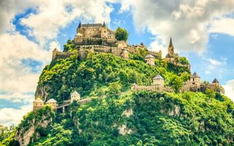 Burg Hochosterwitz auf einem steilen, bewaldeten Hügel in Österreich mit Verteidigungsmauern, Türmen und Kirchturm unter bewölktem Himmel.