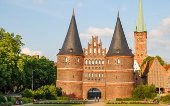 Das Holstentor, ein mittelalterliches Stadttor aus rotem Backstein in Lübeck mit zwei runden Türmen und Kegeldächern, umgeben von Grünflächen.