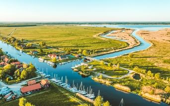 Luftaufnahme des Memeldeltas mit gewundenen Wasserwegen, grünen Feldern, Yachthafen mit Segelbooten und kleinem Dorf mit roten Dächern.