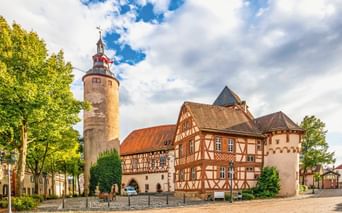 Historische Schlossanlage in Tauberbischofsheim mit rundem Steinturm, Fachwerkhäusern und Kopfsteinpflaster unter blauem Himmel.