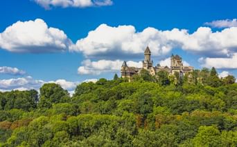 Schloss Braunfels mit Türmen thront auf einem dicht bewaldeten Hügel unter blauem Himmel mit weißen Wolken in Westdeutschland.
