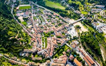 Luftaufnahme von Lamastre, einer französischen Stadt in der Ardèche mit roten Ziegeldächern, umgeben von grünen Feldern und Wäldern mit Fluss.