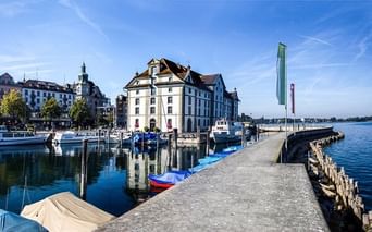 Harbor of Rorschach with historic white buildings, boats moored at the pier, and Lake Constance under blue sky.